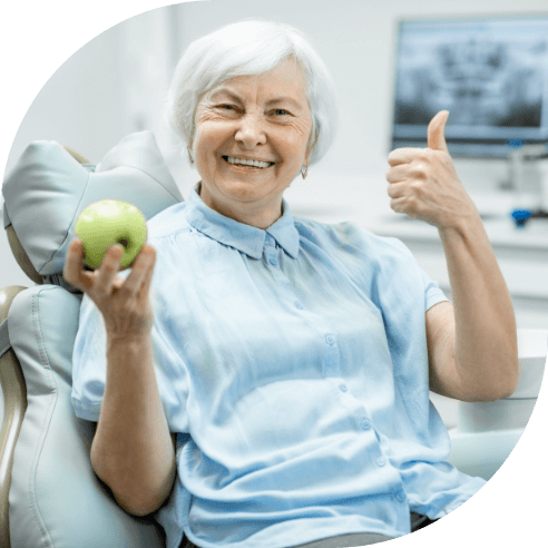 Woman smiling and holding an apple enjoying the benefits of dental implant tooth replacement