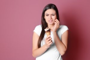 Woman holding ice cream cone, struggling with sensitive teeth